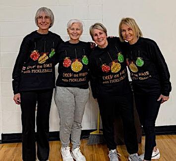 Four members in matching holiday sweaters holding paddles